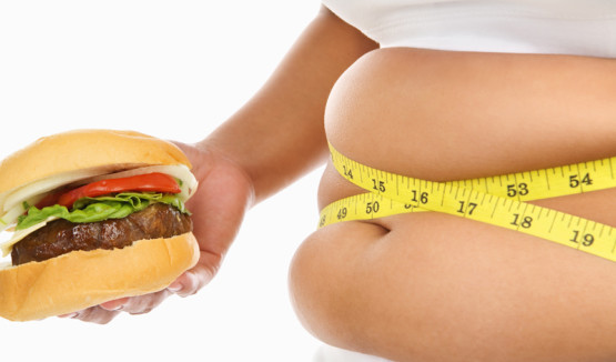 Fat stomach of a woman surrounded with measuring tape with burger over white background